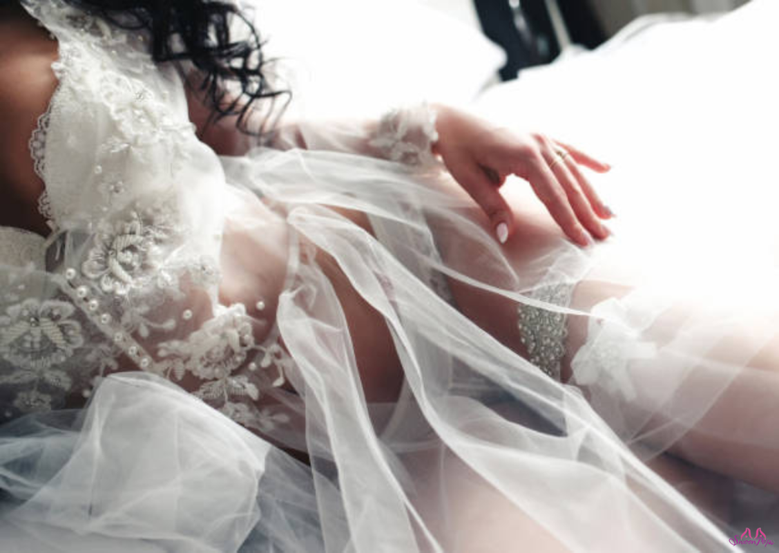 A woman in a wedding dress reclines on a bed, surrounded by decorations for a lingerie bridal shower.